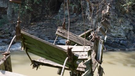A broken bridge made from wood and steel rope over a mountain river